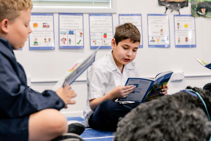 Junior School students learning to read in their classroom with the comforting presence of a therapy dog nearby.